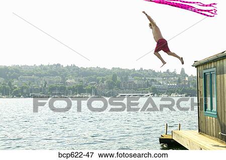 Stock Photo - Man jumping from roof of houseboat with kite. Fotosearch