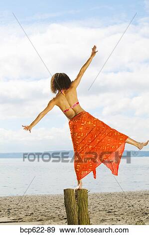 Stock Photo - Woman balancing on log at beach. Fotosearch