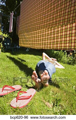 Stock Photograph - Woman lying in grass under drying laundry. Fotosearch