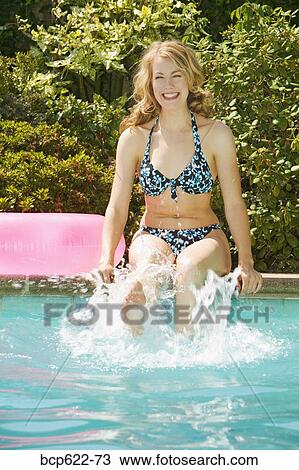 Stock Image - Woman splashing her feet in pool. Fotosearch