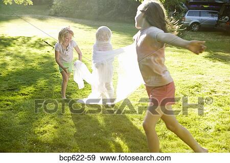Stock Photo - Young girls wrapping friend in fabric outdoors. Fotosearch