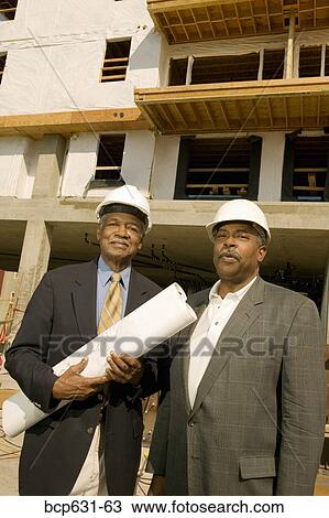 Stock Image - co-worker, afternoon, businessman, business, blueprint, african ethnicity. Fotosearch