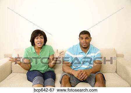 Stock Photo - Confused couple sitting on a couch. Fotosearch