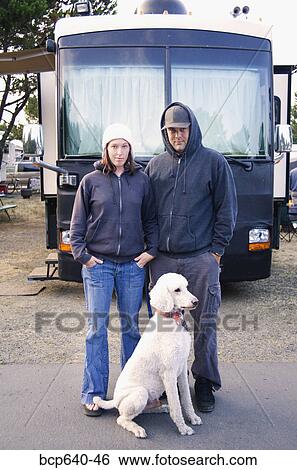 Stock Photograph - Couple and dog standing outside recreational vehicle . Fotosearch