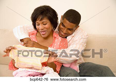 Stock Photograph - Couple examining baby clothes. Fotosearch