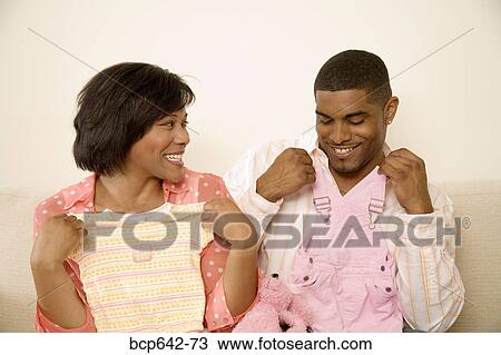 Couple holding baby clothes against themselves View Large Photo Image Stock Image - Couple holding baby clothes against themselves. Fotosearch
