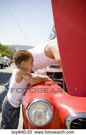 Stock Image - Father and son checking under car hood. Fotosearch