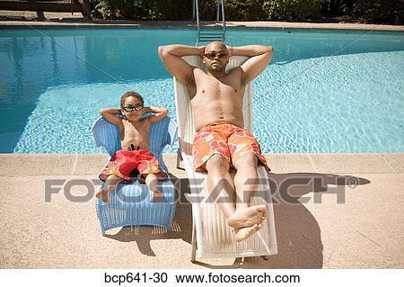 Stock Image - Father and son relaxing by pool. Fotosearch