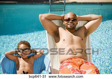 Stock Image - Father and son relaxing by pool. Fotosearch