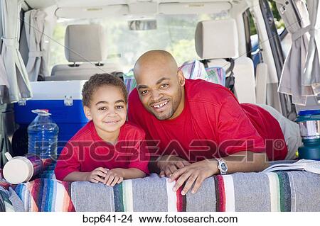 Picture - Father and son sitting in trunk of car with camping gear. Fotosearch