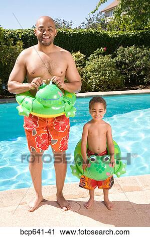 Stock Image - Father and son wearing identical flotation devices by pool. Fotosearch