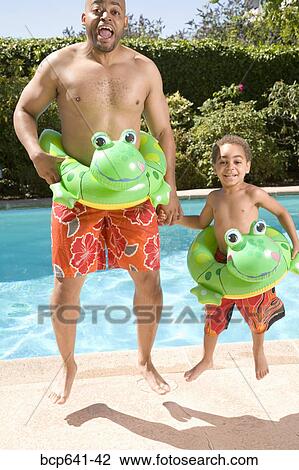 Stock Image - Father and son wearing identical flotation devices by pool. Fotosearch