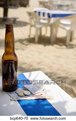 Stock Image - Foreign currency by empty beer bottle on table. Fotosearch