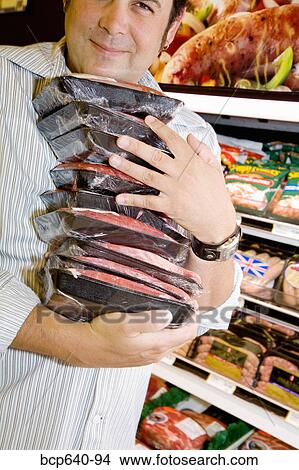 Picture - Man carrying packages of raw meat. Fotosearch