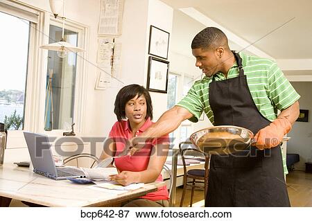 Man cleaning a pan as wife writes checks View Large Photo Image Stock Photo - Man cleaning a pan as wife writes checks. Fotosearch