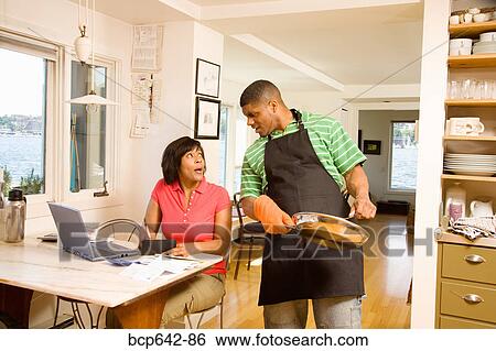 Stock Photograph - Man cleaning a pan as wife writes checks. Fotosearch