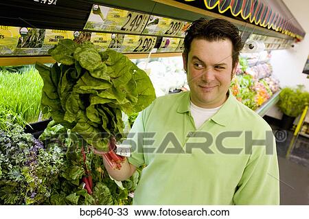 Stock Image - Man wary of green plant in supermarket. Fotosearch