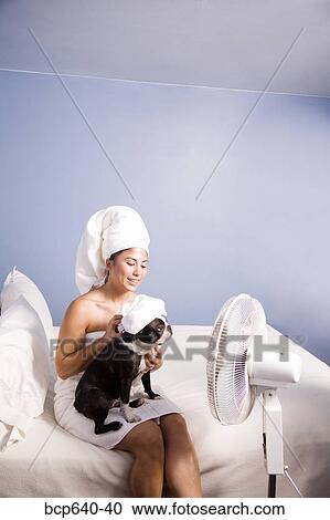 Stock Image - Pacific Islander, Asian woman drying herself and her dog’s hair by fan. Fotosearch