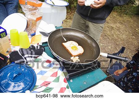 Stock Photo - People cooking breakfast at campsite. Fotosearch