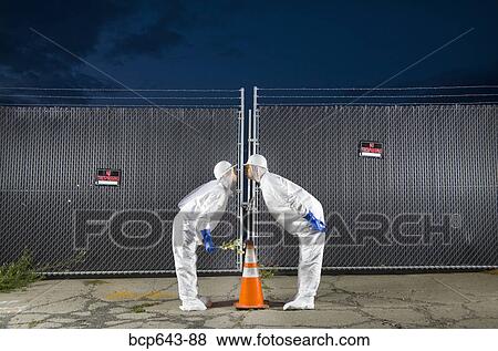 Stock Photo - People in biohazard suits kissing over orange safety cone. Fotosearch
