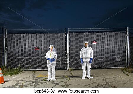 Stock Photo - People in biohazard suits standing outside security gate. Fotosearch