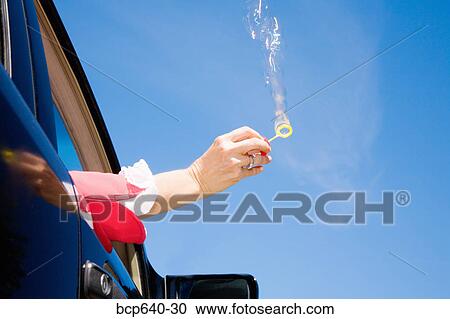 Stock Image - Woman blowing bubbles out car window. Fotosearch