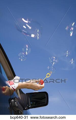 Stock Image - Woman blowing bubbles out car window. Fotosearch