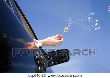 Stock Image - Woman blowing bubbles out car window. Fotosearch