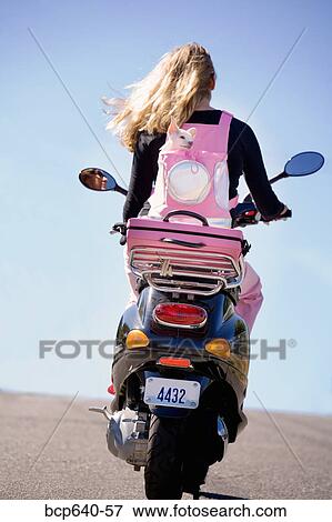 Stock Photo - Woman carrying her small dog on a scooter. Fotosearch