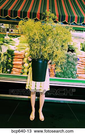 Stock Image - Woman carrying large potted plant in supermarket. Fotosearch