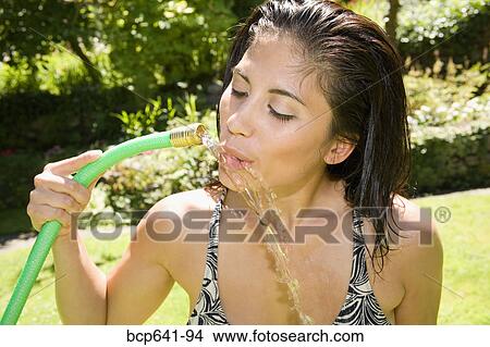 Woman drinking from hose in her backyard View Large Photo Image Picture - Woman drinking from hose in her backyard. Fotosearch