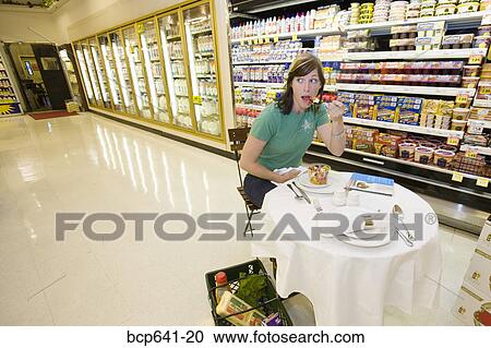 Stock Image - Woman eating dinner in grocery store. Fotosearch