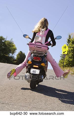 Stock Image - Woman riding a scooter with extended legs. Fotosearch