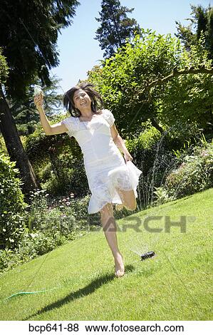 Woman running through sprinkler in her backyard View Large Photo Image Stock Photo - Woman running through sprinkler in her backyard. Fotosearch