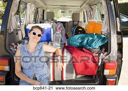 Stock Image - Woman sitting in trunk of car with camping gear. Fotosearch