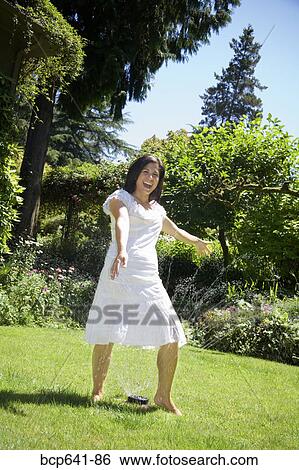 Woman standing in sprinkler in her backyard View Large Photo Image Stock Photograph - Woman standing in sprinkler in her backyard. Fotosearch