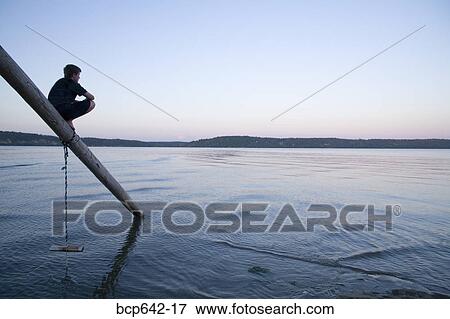 Stock Photo - Young boy balancing on pole extending into lake. Fotosearch