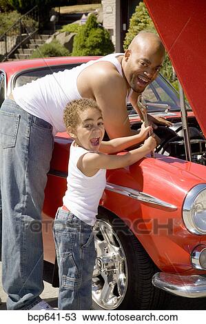 Stock Image - Young boy helping his father work on car. Fotosearch