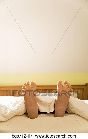 Stock Photo - Bare feet sticking out from blanket. Fotosearch