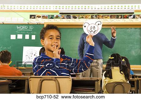 Stock Image - Boy holding drawing over teacher’s face. Fotosearch