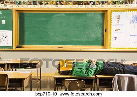 Boy laying on classroom desks with book over face View Large Photo Image Stock Image - Boy laying on classroom desks with book over face. Fotosearch