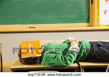 Boy laying on classroom desks with book over face View Large Photo Image Stock Photo - Boy laying on classroom desks with book over face. Fotosearch