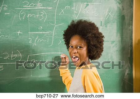 Stock Photo - Boy sticking out tongue and writing on blackboard. Fotosearch