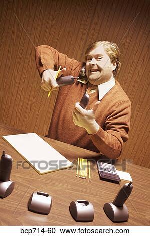 Stock Image - Businessman at desk using multiple telephones. Fotosearch