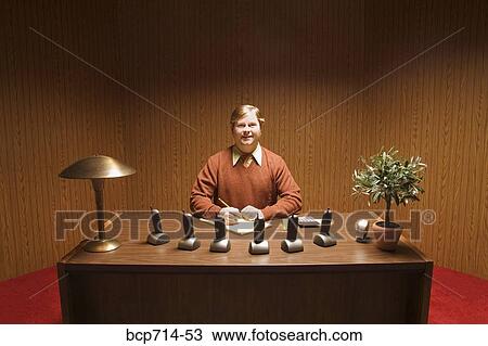 Stock Image - Businessman at desk with multiple telephones. Fotosearch