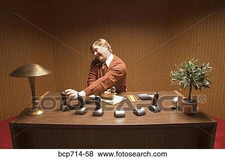 Stock Photo - Businessman at desk with multiple telephones. Fotosearch