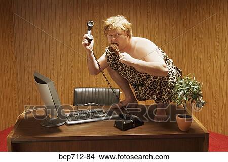Picture - Businessman dressed as caveman crouching on desk. Fotosearch