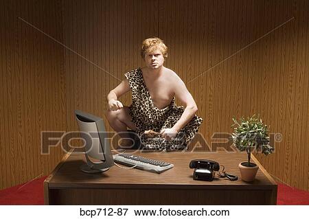 Businessman dressed as caveman crouching at desk View Large Photo Image Stock Photo - Businessman dressed as caveman crouching at desk. Fotosearch