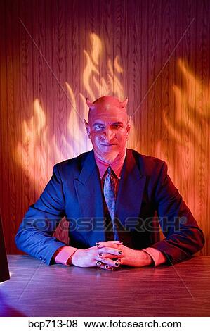 Businessman dressed as devil at desk View Large Photo Image Stock Photo - Businessman dressed as devil at desk. Fotosearch