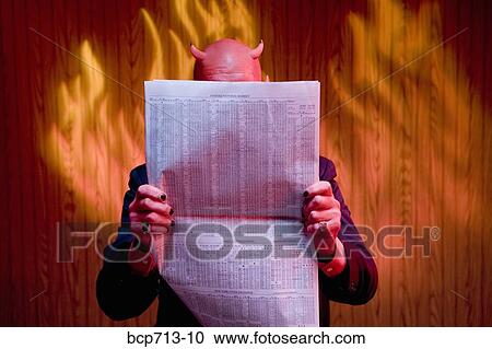 Stock Image - Businessman dressed as devil reading newspaper. Fotosearch